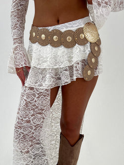 Person wearing a white lace dress with decorative belt and brown boots on a plain background