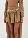 Person wearing a camel skort with a gold belt on a white background