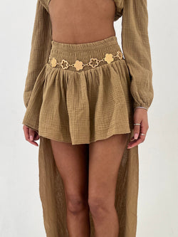 Person wearing a camel skort with a gold belt on a white background