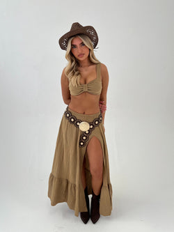 woman in a camel outfit with brown boots, belt and hat on a white background