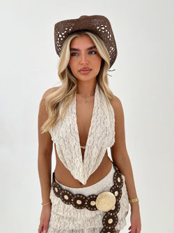Woman wearing a beige lace top, brown hat, and decorative belt on a white background