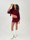 Lady in a burgundy outfit with white hat and boots on a white background