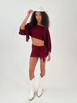 Lady in a burgundy outfit with white hat and boots on a white background