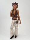 Woman wearing a cowboy outfit with a vest, pants, and hat on a white background