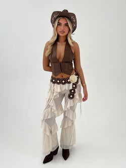 Woman wearing a cowboy outfit with a vest, pants, and hat on a white background
