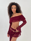 Lady wearing burgundy lace top and skirt with a gold belt on a white background