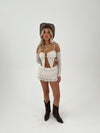 Woman wearing a beige lace outfit with brown boots and hat on a white background
