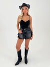 Woman wearing a black bodysuit, denim shorts, and black cowboy boots on a white background