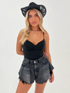 Woman wearing a black crop top and denim shorts with a black crochet hat on a white background