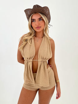 Woman wearing a beige sleeveless top and shorts with a matching hat on a white background