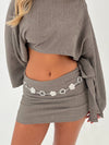 Person wearing a gray ribbed sweater and skirt with a chain detail on a white background