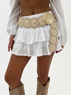 White skirt with gold embellishments and beige boots on a plain background